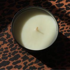 a white candle sitting on top of a leopard print table cloth next to a black cup