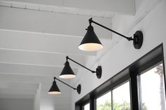 three black and white lights hanging from the ceiling in a room with two large windows