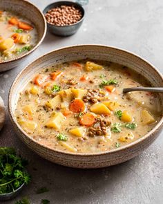 two bowls filled with soup on top of a table next to some bread and vegetables