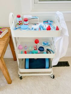 a white cart filled with lots of items on top of a floor next to a wooden table