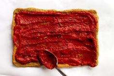 a piece of bread with red spread on top and a spoon in the middle next to it