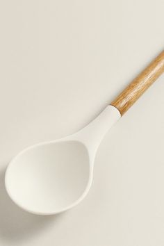 a white spoon sitting on top of a table next to a wooden spoon with a wood handle