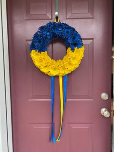 a blue and yellow wreath hanging on the front door to a purple door with flowers