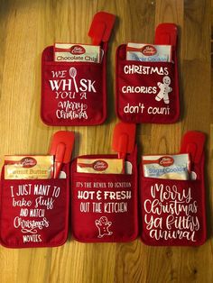 four red oven mitts with christmas sayings on them sitting on a wooden table