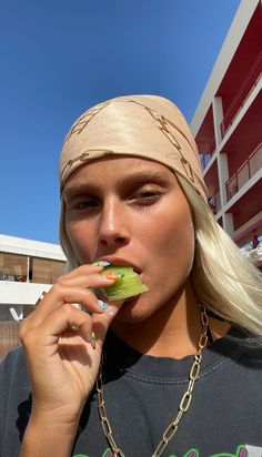 a woman with blonde hair wearing a bandana and eating something in front of a building