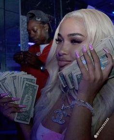 lady with pink nail polish holding money in front of her face while another man looks on