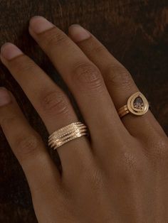 a woman's hand with two gold rings on top of her finger and an engagement ring in the middle