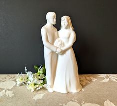 a statue of two people holding hands next to white flowers on a tableclothed surface