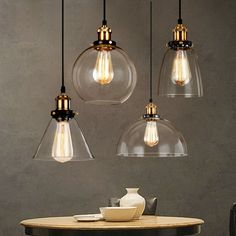 three clear glass pendant lights hanging from the ceiling above a table with a phone on it