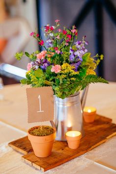 a vase filled with flowers sitting on top of a wooden table next to candles and a sign