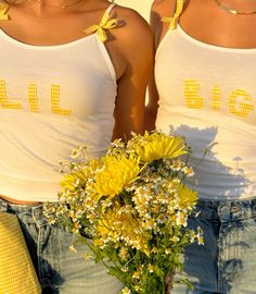 two women in white tank tops holding yellow flowers