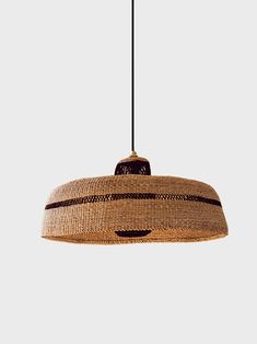 a woven light shade hanging from a black cord on a white wall with an orange and brown stripe design