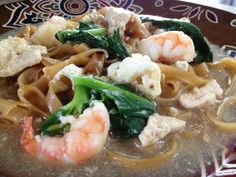 a bowl filled with noodles, shrimp and broccoli on top of a table