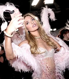 a woman taking a selfie with her cell phone in front of some pink feathers