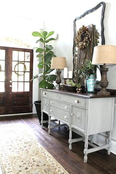 a white dresser with two lamps on top and a mirror above it in a living room