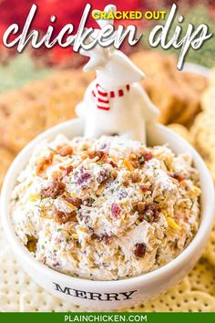 a white bowl filled with chicken dip surrounded by crackers and christmas decorations on the side