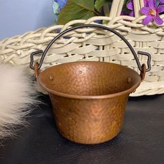 a metal bucket sitting on top of a table next to a basket with flowers in it