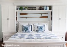 a white bed with blue and white pillows in a room that has built - in bookshelves