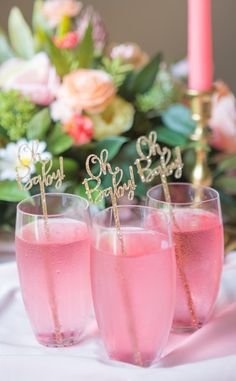 three glasses filled with pink liquid sitting on top of a table next to a candle