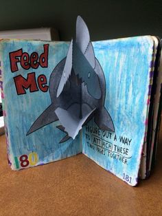 an open book with a shark on it and the title feed me written in red