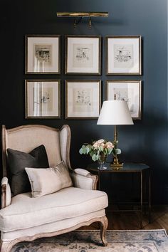 a living room with pictures on the wall and a chair next to a lamp in front of it