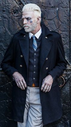 an older man with white hair wearing a coat and tie standing in front of a door