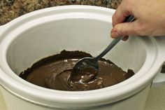 a person is stirring chocolate into a white crock pot with a spoon in it