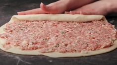 someone is kneading the dough for an uncooked pizza crust with meat on it