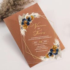 an orange and gold wedding card with flowers on the front is sitting next to some feathers