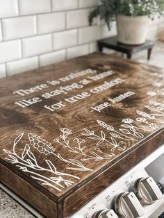 a wooden cutting board sitting on top of an oven in a kitchen next to a potted plant