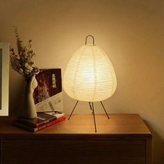 a white lamp sitting on top of a wooden table next to a book and vase