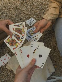 two hands holding playing cards while sitting on the ground