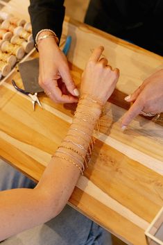 two people sitting at a table with bracelets on their arm and one person reaching for something