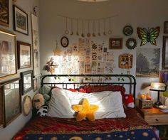 a bedroom with many pictures on the wall and a teddy bear laying on the bed