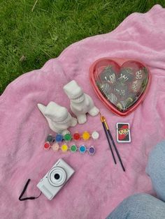 the contents of a heart shaped box are laid out on a pink blanket next to a camera