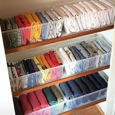 an organized closet filled with folded shirts and other items in clear bins on wooden shelves