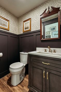 a white toilet sitting next to a sink in a bathroom under two framed pictures on the wall