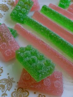 some gummy bears are sitting on a white and gold plate with pink and green candies