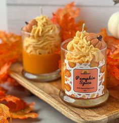 two small candles sitting on top of a wooden tray filled with pumpkins and leaves