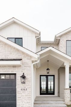 a white house with black front doors and two lights on each side of the door