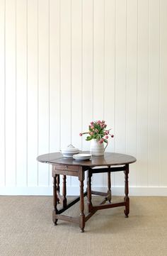 a vase with flowers sitting on top of a wooden table next to a white wall