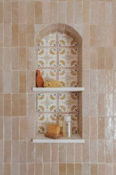 two white shelves in the corner of a tiled wall with various items on them,