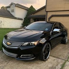 a black chevrolet camaro parked in front of a house with grass and two garage doors