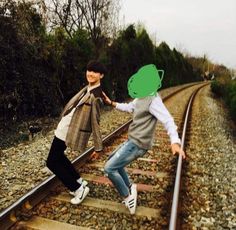 two young men standing on train tracks holding hands with each other and smiling at the camera