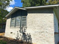 a brick house with green shutters and trees in the background