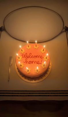 a welcome home cake with lit candles on the front and side, surrounded by forks and knives