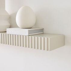 an egg sitting on top of a book next to a white vase and other items