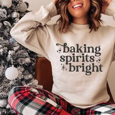 a woman sitting in front of a christmas tree wearing a sweatshirt and plaid pants with merry bright written on it