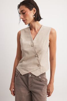 This vest features a relaxed fit and an asymmetrical design. It has a v neckline and a button closure down the front. Beige V-neck Vest With Buttons, Sleeveless Beige Vest With Buttons, Beige Sleeveless Vest With Buttons, Classic Beige Vest Top, Beige Workwear Vest With Button Closure, Beige Button Closure Vest For Work, Beige V-neck Tank Top For Work, Beige V-neck Vest For Work, Classic Beige V-neck Vest