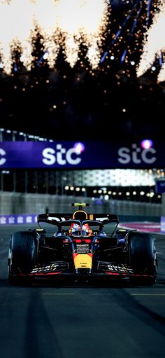 a red and yellow race car driving on a track at night with fireworks in the background